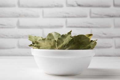 Photo of Dry bay leaves in bowl on white wooden table