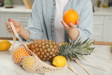 Photo of Woman with string bag of fresh fruits at light marble table, closeup