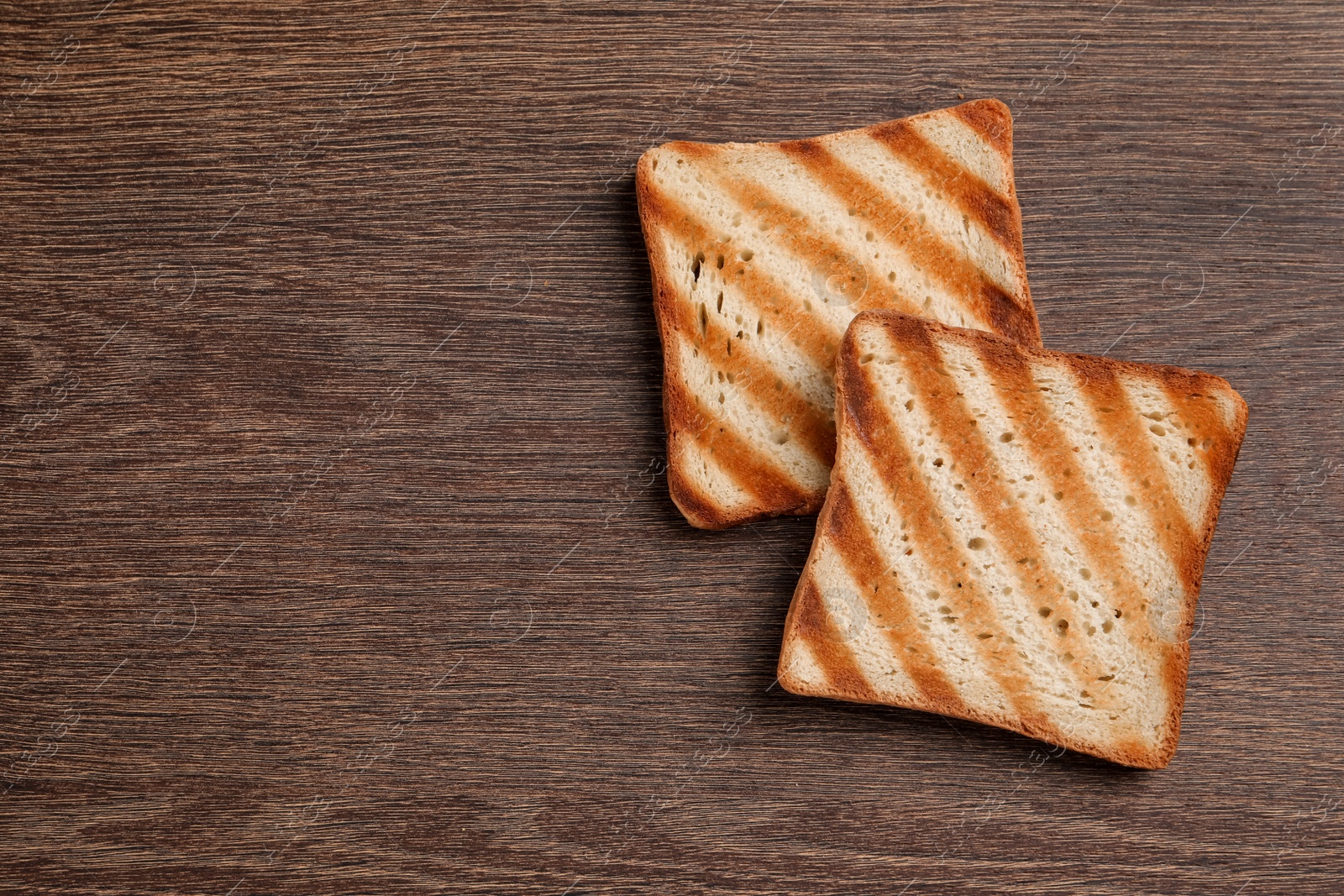 Photo of Slices of delicious toasted bread on wooden table, top view. Space for text