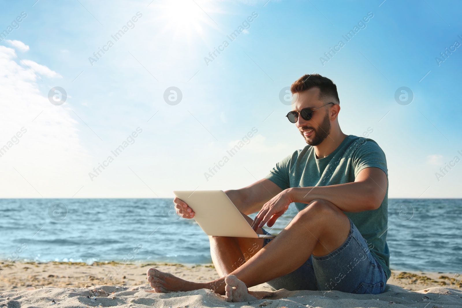 Photo of Man working with laptop on beach. Space for text