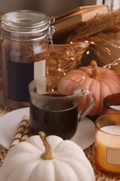Cup of hot drink and pumpkins on wicker mat indoors