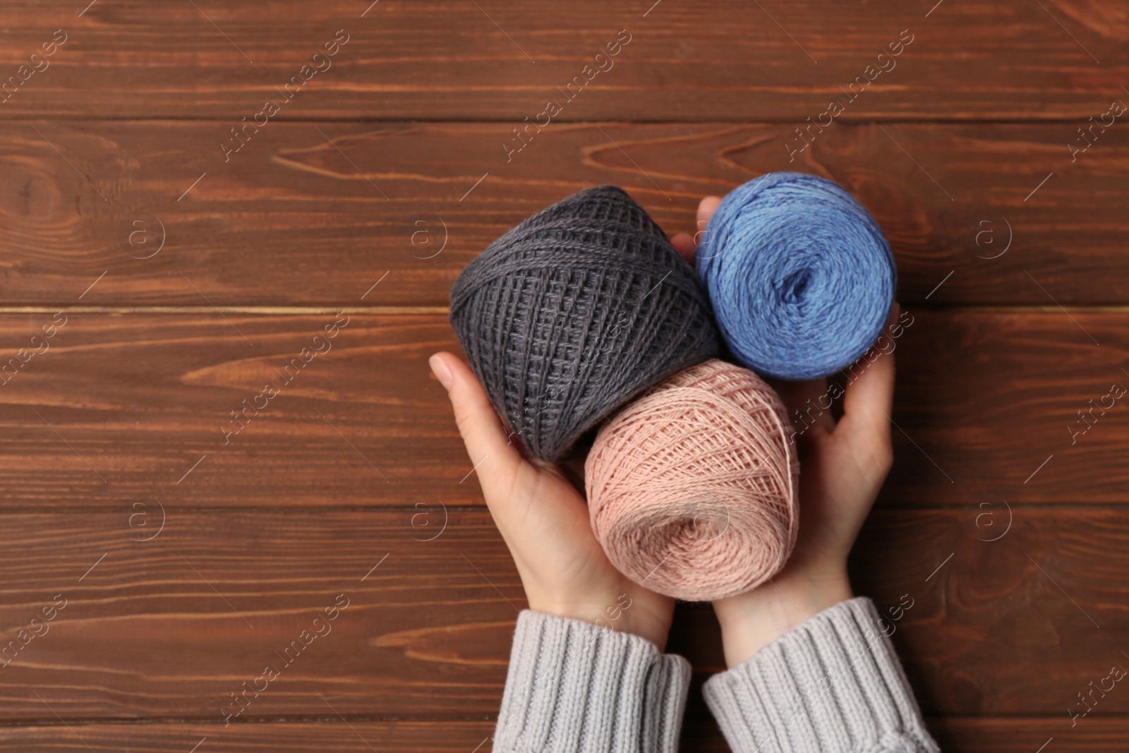 Photo of Woman holding clews of threads on wooden background, top view. Space for text