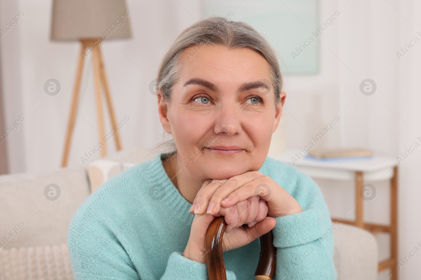 Photo of Senior woman with walking cane sitting on sofa at home