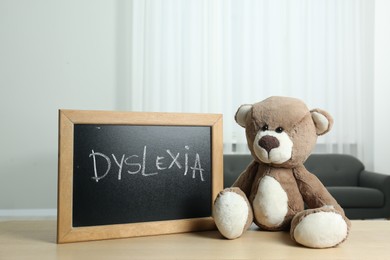 Photo of Teddy bear and small blackboard with word Dyslexia on wooden table indoors
