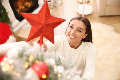 Woman decorating Christmas tree with star topper in room