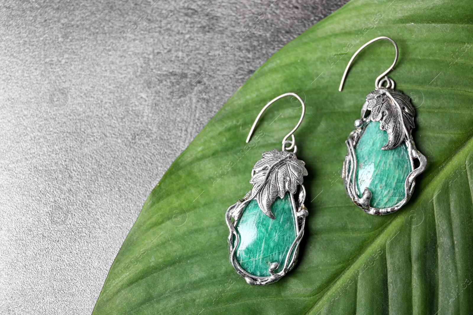 Photo of Beautiful pair of silver earrings with amazonite gemstones on green leaf, above view. Space for text