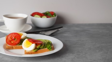 Photo of Tasty sandwiches with boiled egg, avocado and tomato served on grey table, space for text