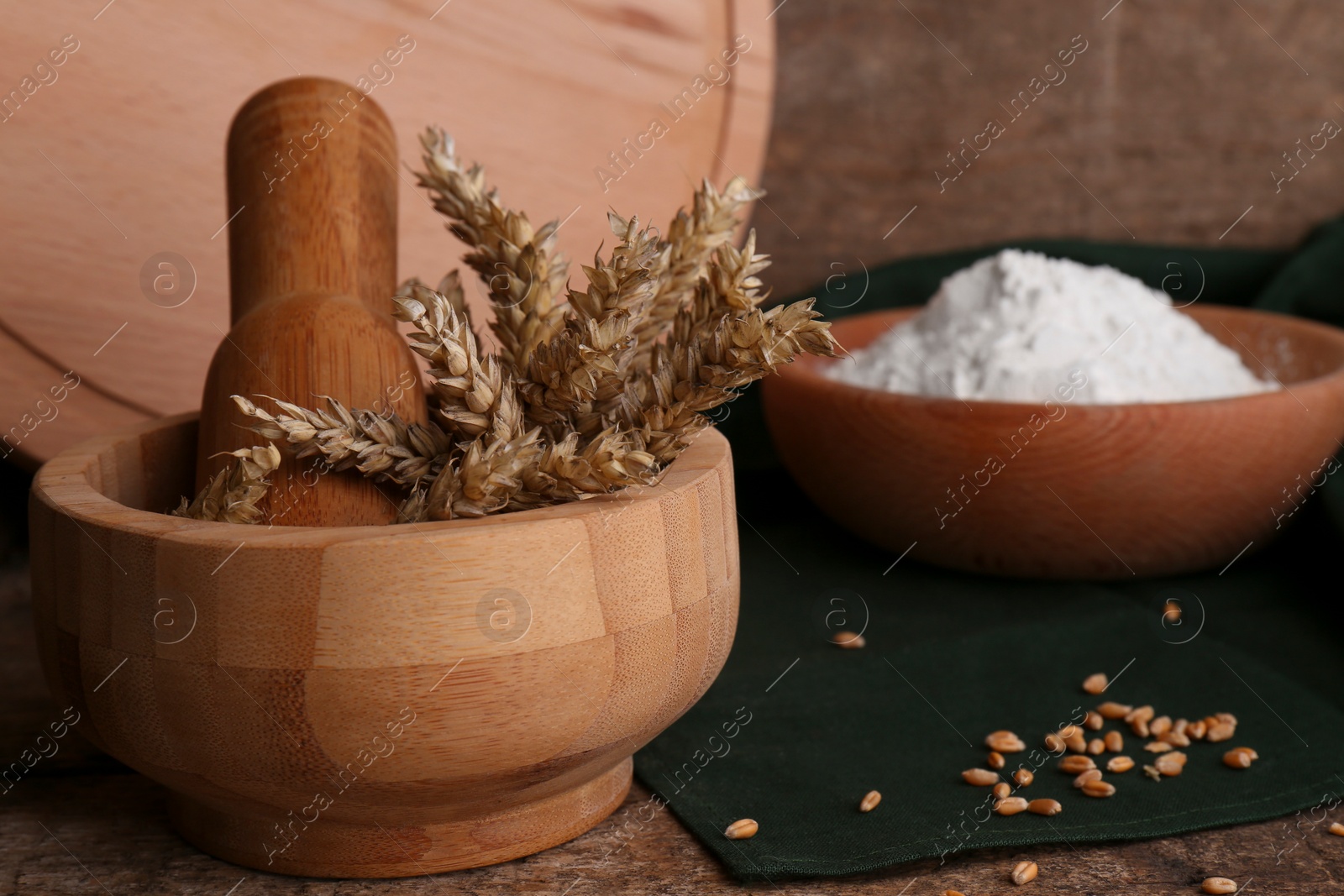 Photo of Mortar with spikes and bowl of wheat flour on wooden table, space for text