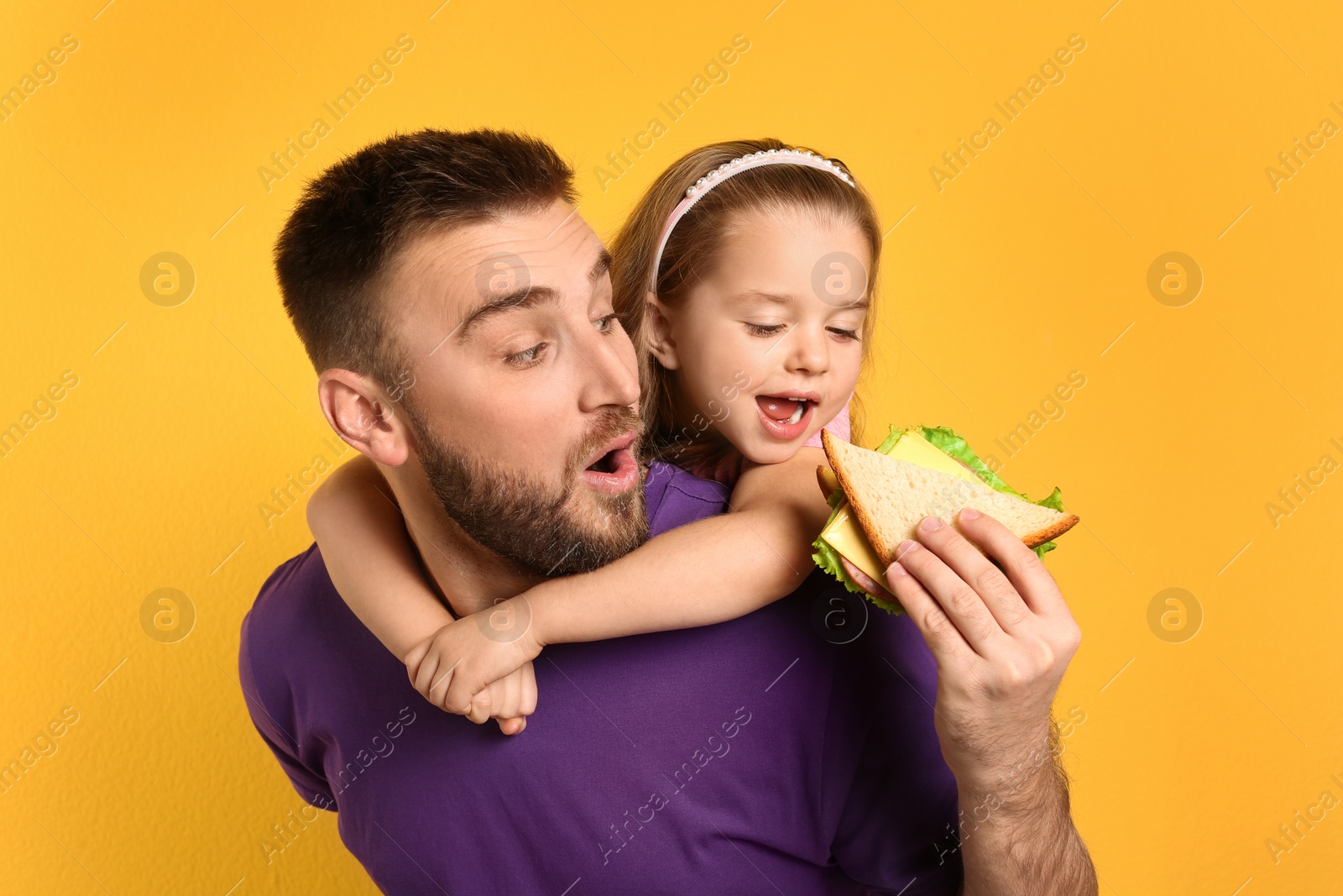 Photo of Young man and his daughter with sandwich on yellow background