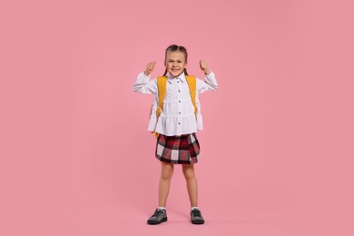 Happy schoolgirl with backpack on pink background