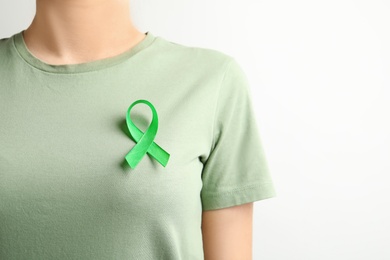 Photo of Woman with green ribbon on t-shirt against light background. Cancer awareness