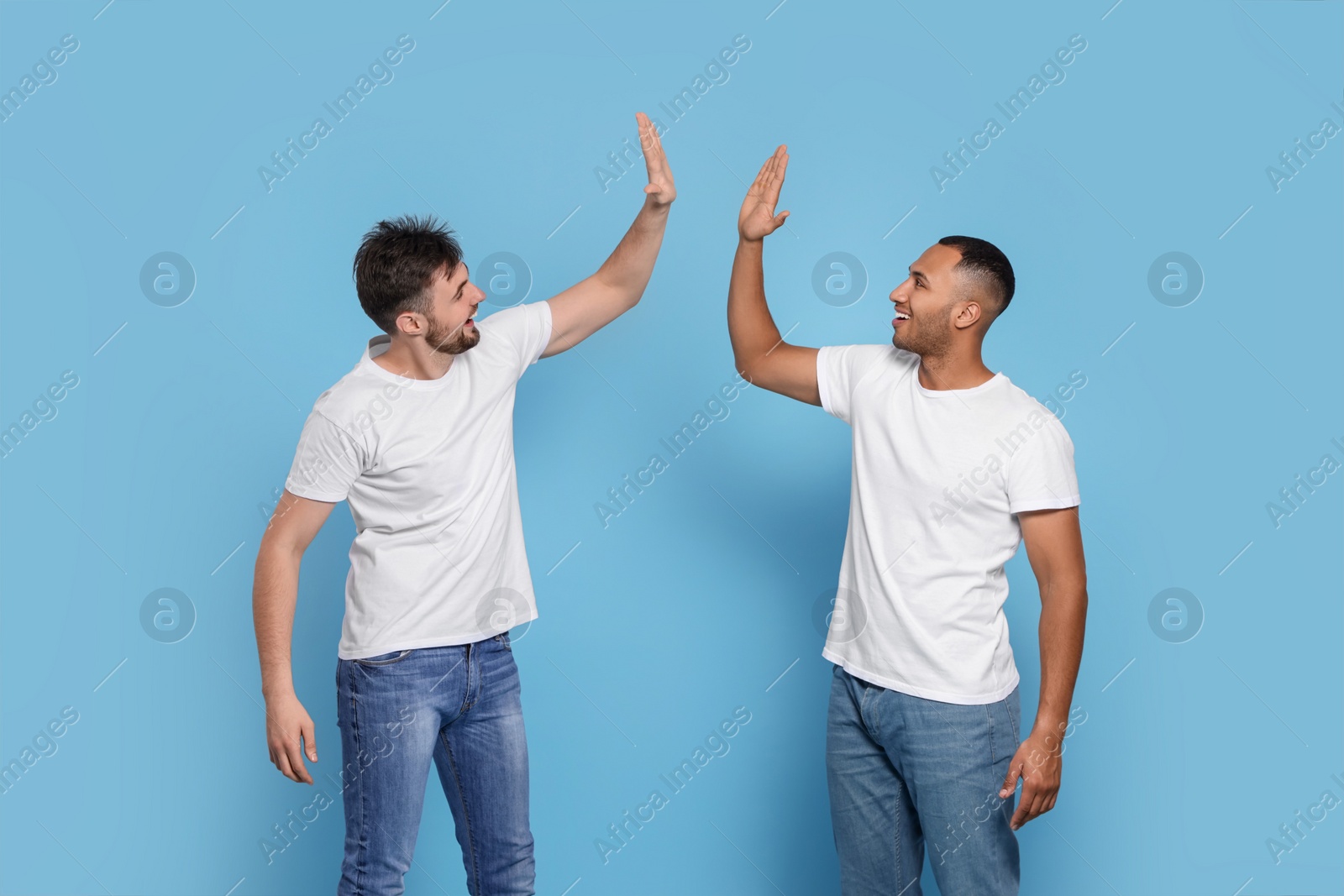 Photo of Men giving high five on light blue background