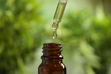 Photo of Pipette and bottle of essential oil on blurred background, closeup