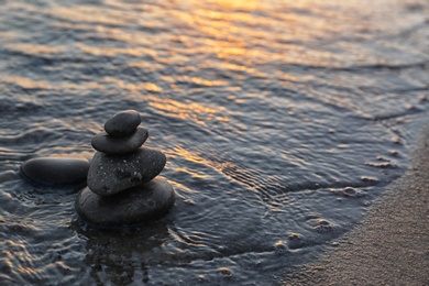 Photo of Dark stones on sand near sea at sunset, space for text. Zen concept