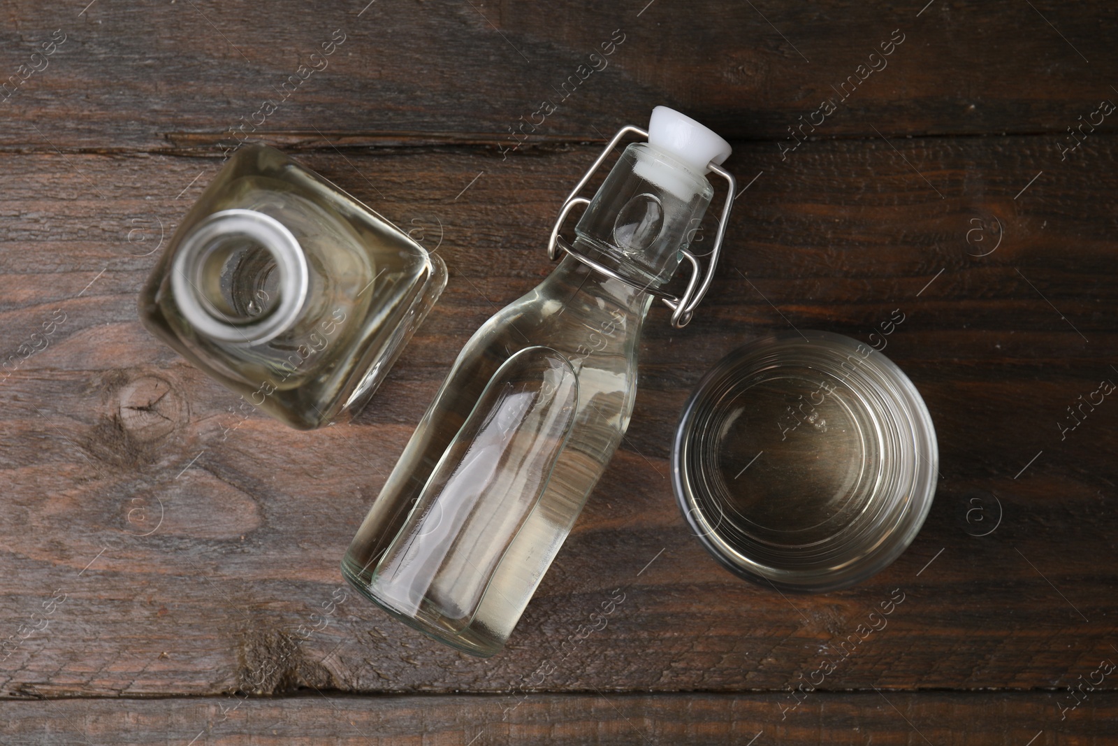 Photo of Vinegar in bottles and glass on wooden table, flat lay