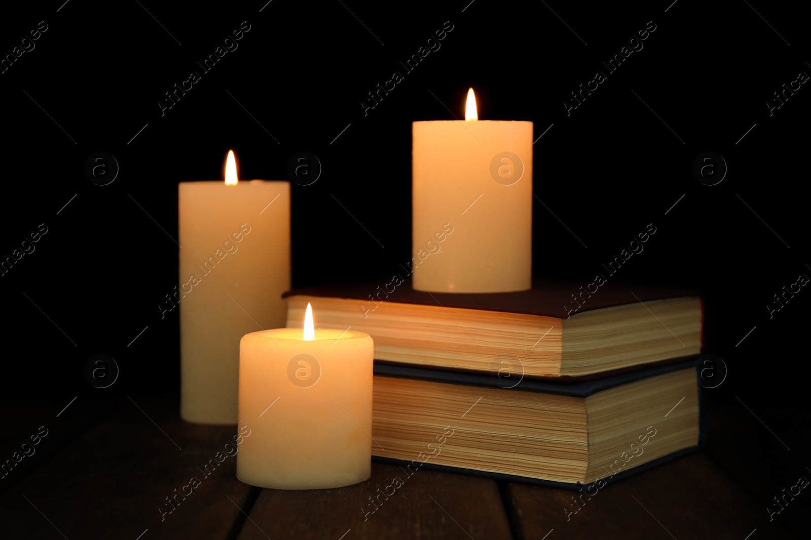 Photo of Burning candles and stack of books on wooden table in darkness