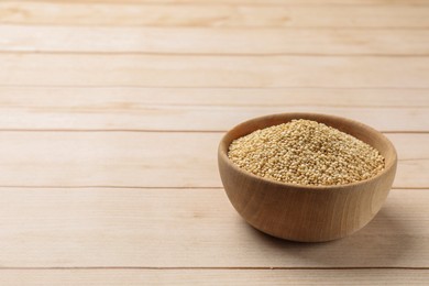 Photo of Raw quinoa in bowl on wooden table, space for text