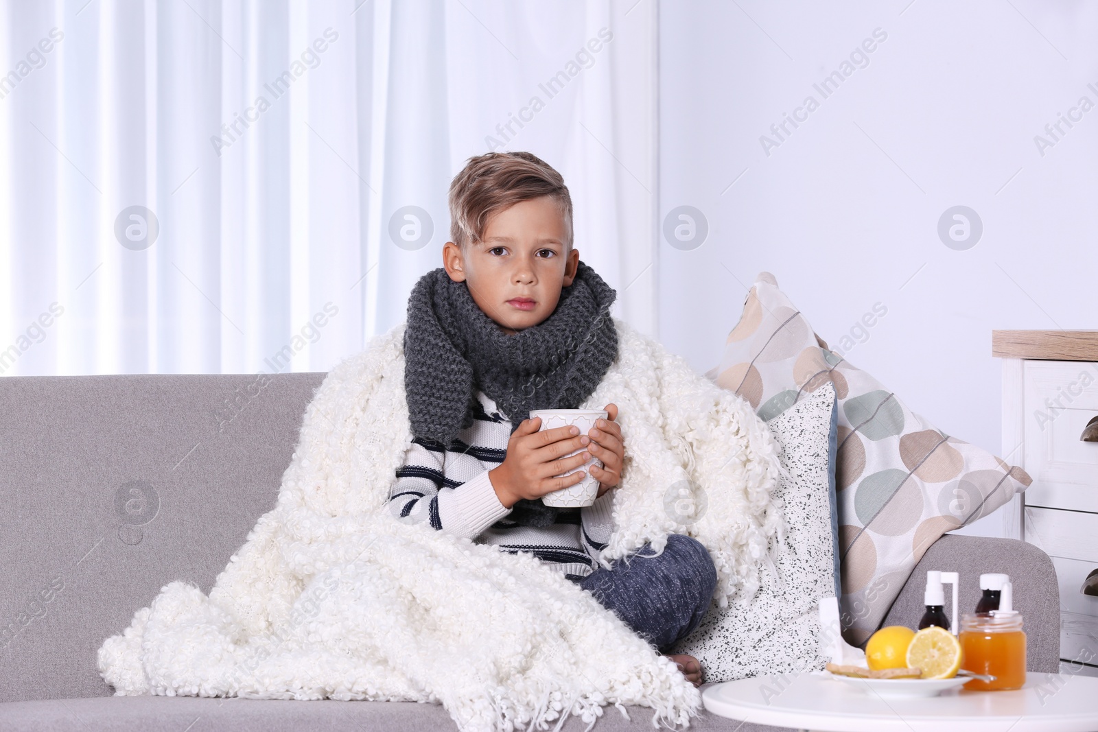 Photo of Ill little boy with cup of hot tea for cough on sofa