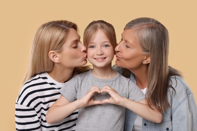 Photo of Three generations. Happy grandmother, her daughter and granddaughter making heart with hands on beige background