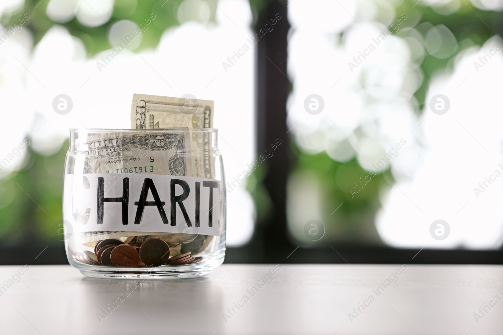 Photo of Glass jar with money and word CHARITY on table against blurred background, space for text