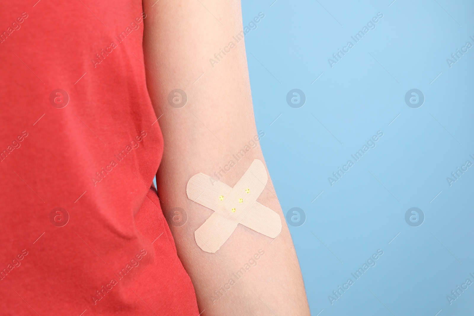 Photo of Blood donation. Woman with sticking plaster on her arm against light blue background, closeup. Space for text
