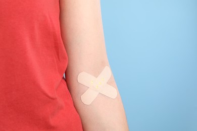 Photo of Blood donation. Woman with sticking plaster on her arm against light blue background, closeup. Space for text