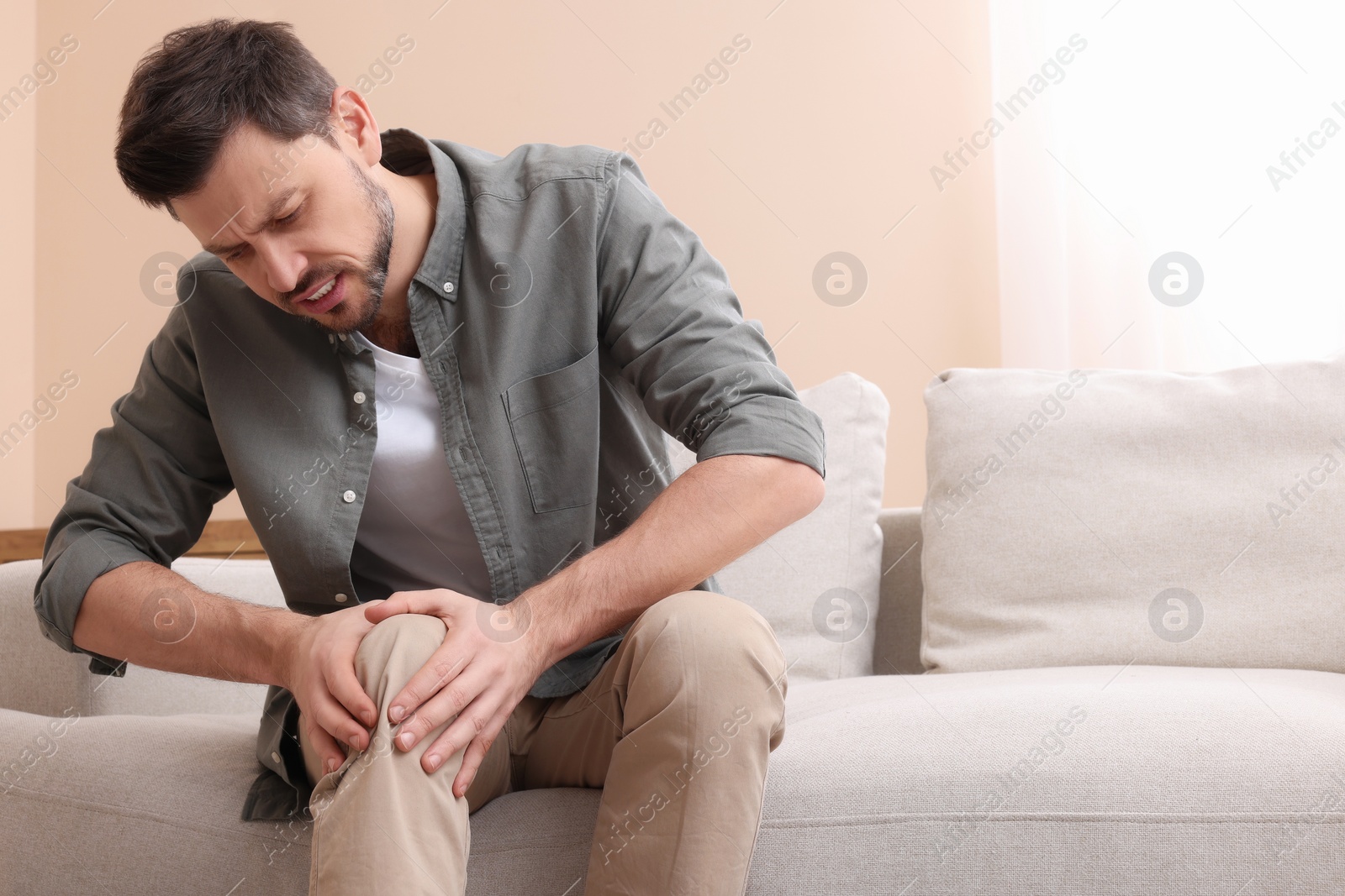 Photo of Man suffering from pain in his leg at home, space for text. Arthritis symptoms