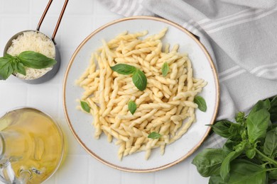 Plate of delicious trofie pasta with basil leaves on white tiled table, flat lay