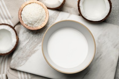 Photo of Bowl of delicious coconut milk, flakes and coconuts on light grey table, flat lay