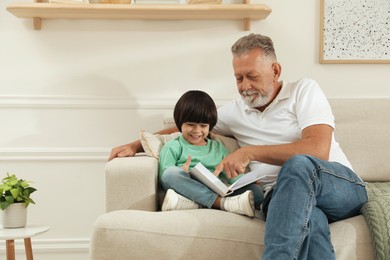 Happy grandfather with his grandson reading book together at home