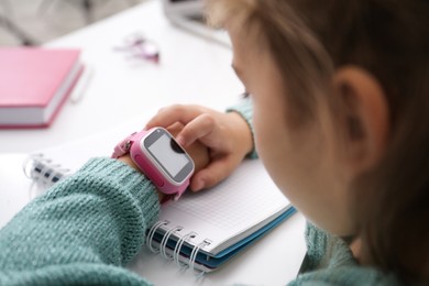 Photo of Girl with stylish smart watch at table, closeup