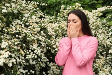 Woman suffering from seasonal pollen allergy near blossoming tree on spring day