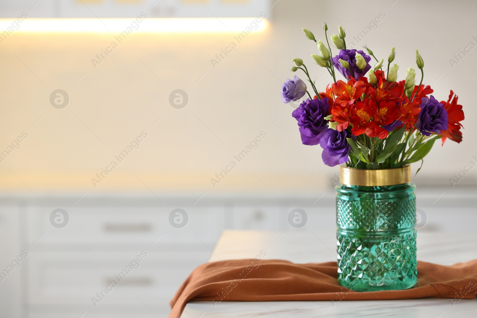 Photo of Glass vase with fresh flowers and towel on table in kitchen. Space for text