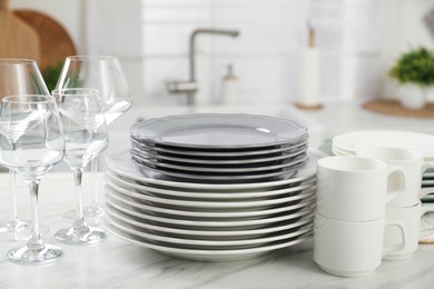 Photo of Clean plates, cups and glasses on white marble table in kitchen