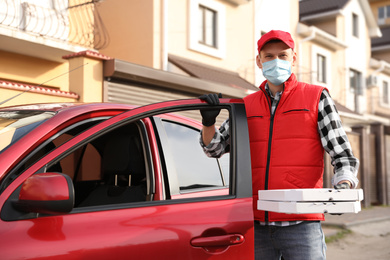 Photo of Courier in protective mask and gloves with pizza boxes near car outdoors. Food delivery service during coronavirus quarantine