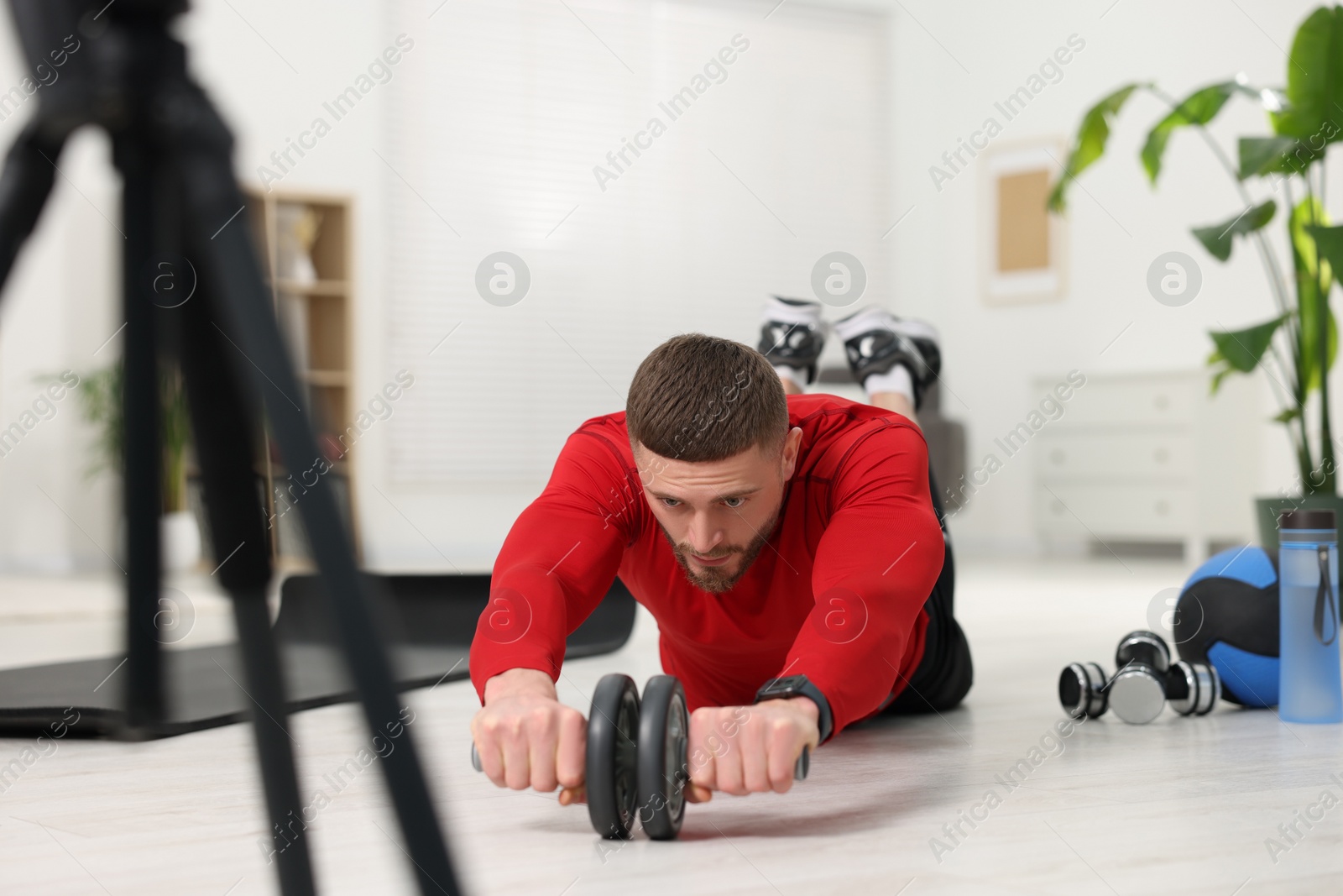 Photo of Trainer with ab wheel recording workout on camera at home