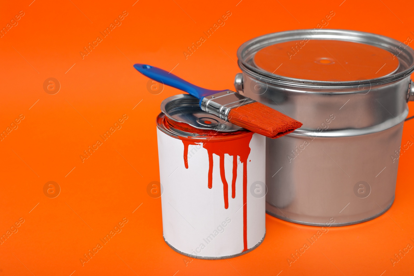 Photo of Cans of orange paint and brush on color background. Space for text