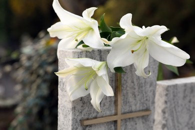 Photo of White lilies on granite tombstone outdoors. Funeral ceremony