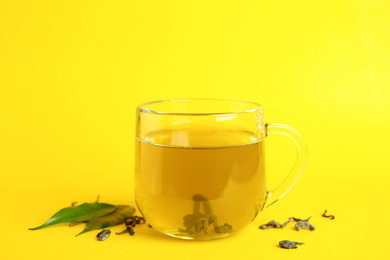 Photo of Cup of green tea and leaves on yellow background