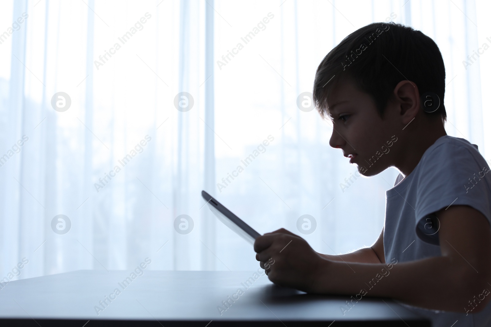 Photo of Shocked child with tablet at table indoors. Danger of internet