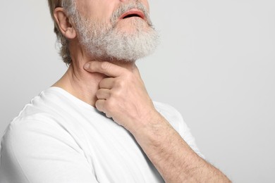 Senior man suffering from sore throat on white background, closeup view with space for text. Cold symptoms