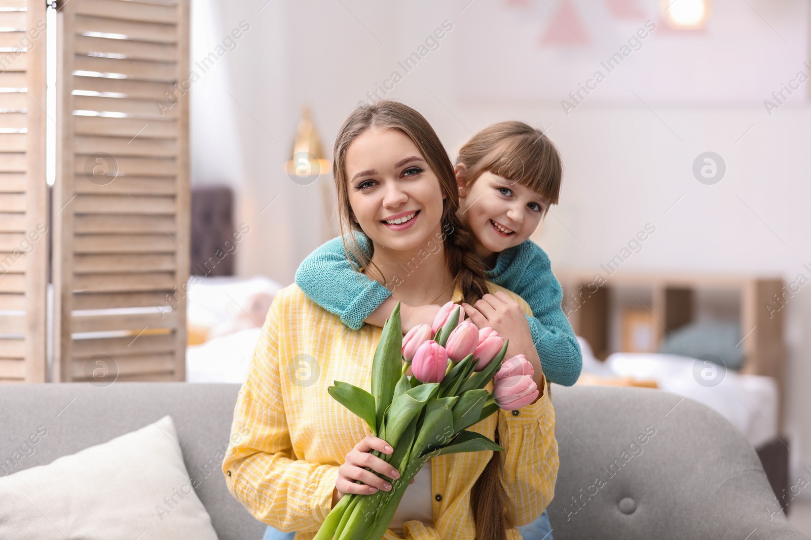 Photo of Happy mother and daughter with flower bouquet at home. International Women's Day