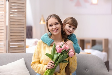 Photo of Happy mother and daughter with flower bouquet at home. International Women's Day