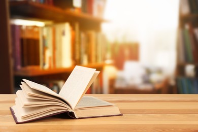 Open book on wooden table in library. Space for text 