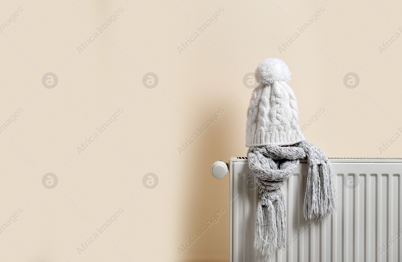 Photo of Knitted cap and scarf on heating radiator indoors