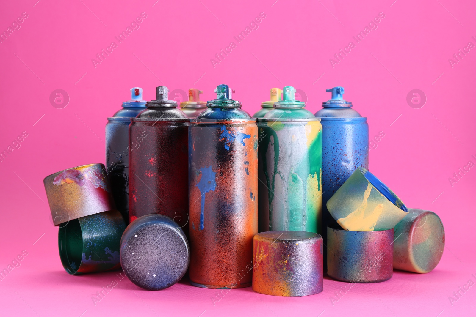 Photo of Many spray paint cans with caps on pink background