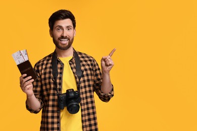 Photo of Smiling man with passport, tickets and camera pointing at something on yellow background. Space for text