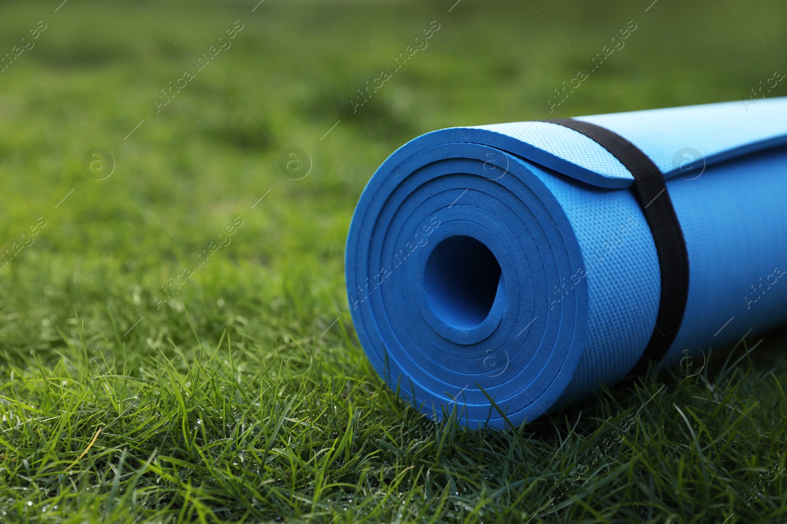 Photo of Bright karemat or fitness mat on fresh green grass outdoors, closeup. Space for text