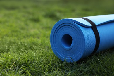 Photo of Bright karemat or fitness mat on fresh green grass outdoors, closeup. Space for text