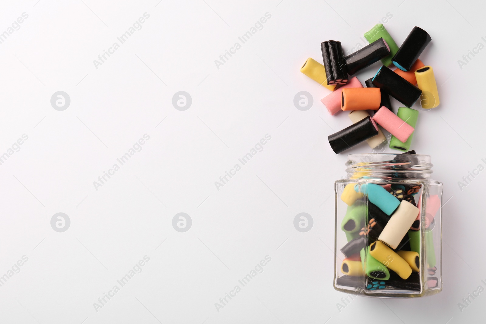 Photo of Glass jar of tasty liquorice candies on light background, top view. Space for text